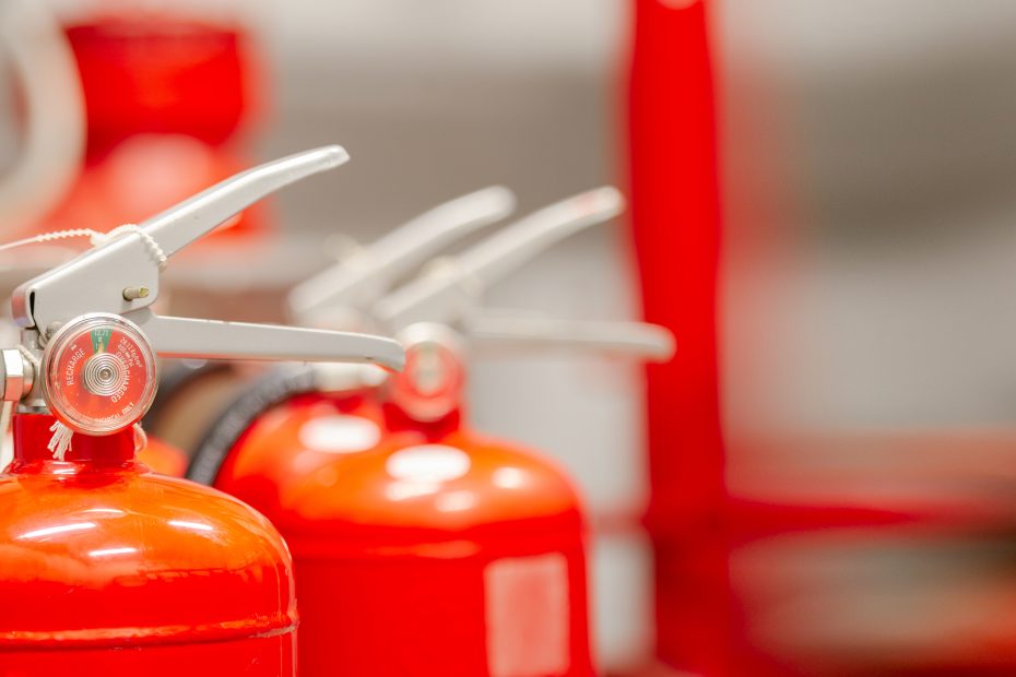 New fire extinguishers with beaded tamper-evident ties around the squeeze levers lined up in a row against a blurry background.
