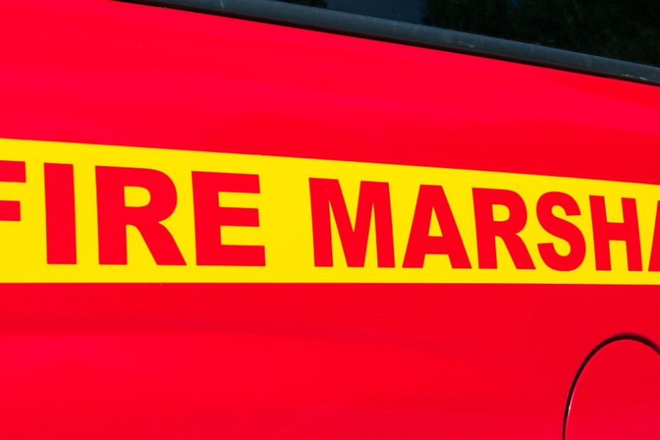 The side of a red truck features a yellow stripe with "Fire Marshal" written in bold, all-capital red letters.